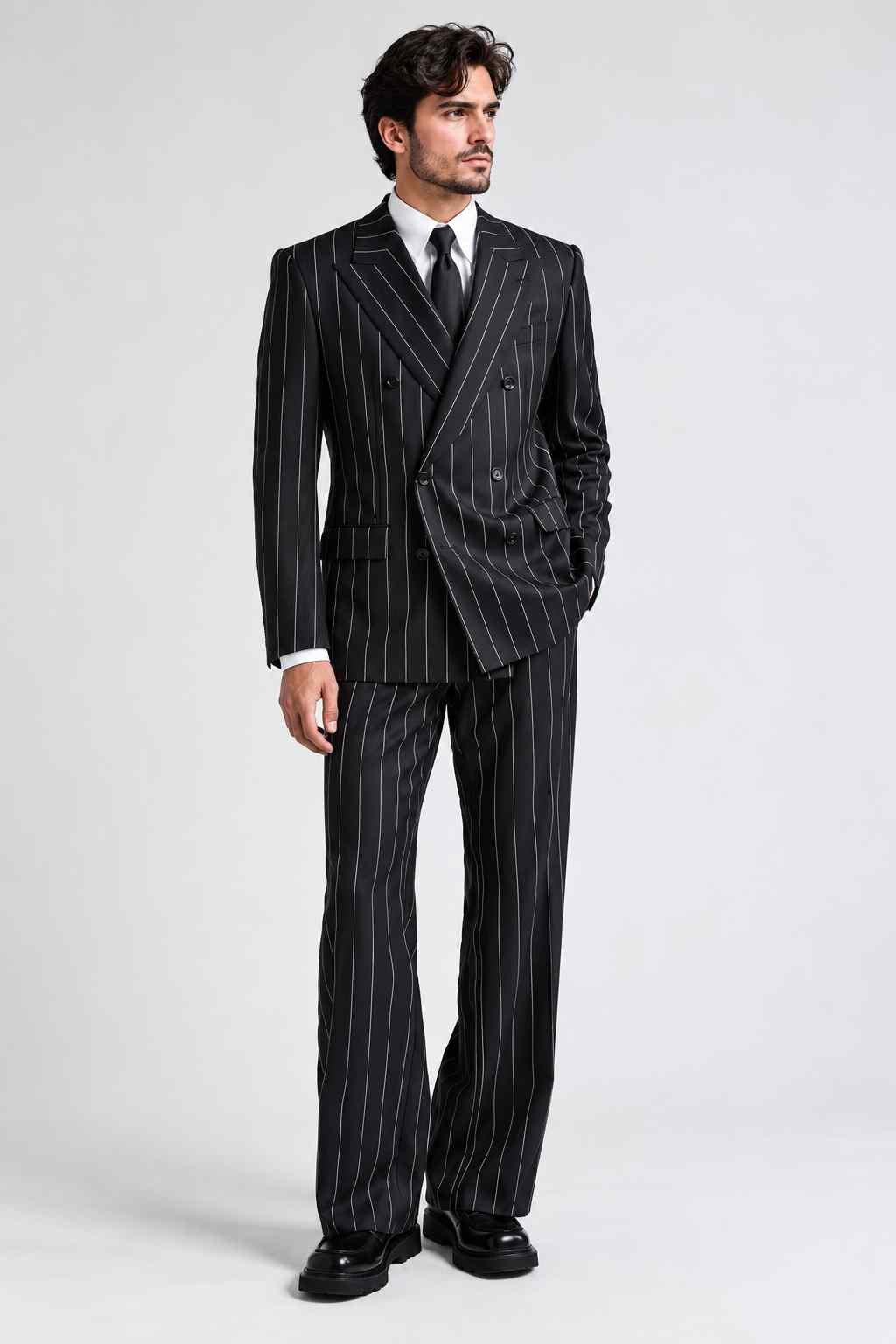 Full-length view of a man wearing a black pinstripe double-breasted suit with white stripes, wide peak lapels, a white shirt, and black tie.