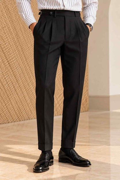 Men's black high-waisted pleated trousers with a tailored fit, belt fastening and cuffed hems, styled with a white striped shirt and black loafers.