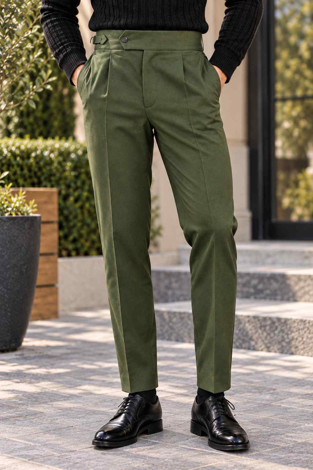 Men's olive green Gurkha trousers featuring a high waist, front pleats, adjustable side buckles and turn-up cuffs, styled with a black turtleneck.