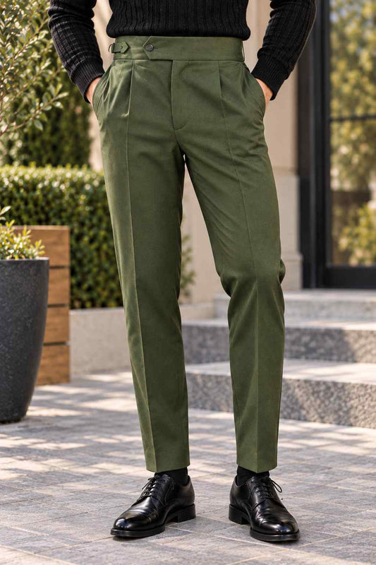 Men's olive green Gurkha trousers featuring a high waist, front pleats, adjustable side buckles and turn-up cuffs, styled with a black turtleneck.