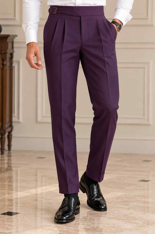 Men's plum purple pleated trousers featuring a high-waisted buckle waistband and tailored fit, styled with a white shirt and black dress shoes.